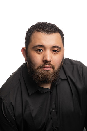A young man poses for a headshot against a white background inside the studio.